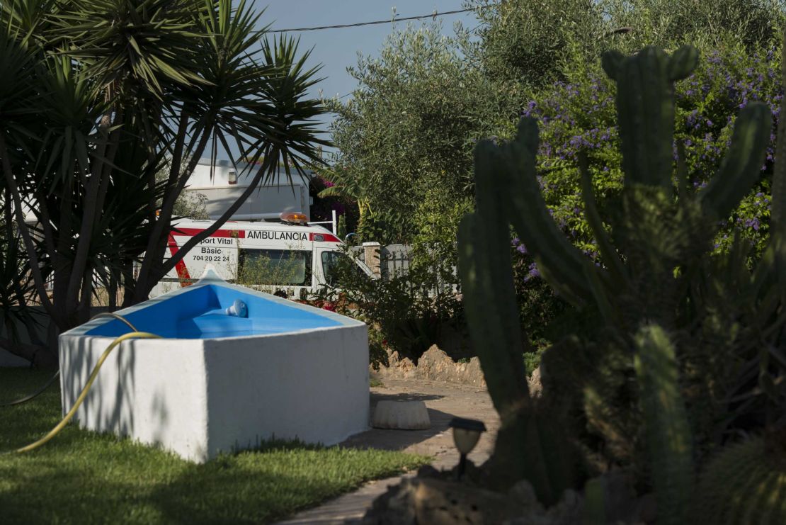 An ambulance is seen through a neighbor's front lawn, where a hose dangles in a half-empty pool.