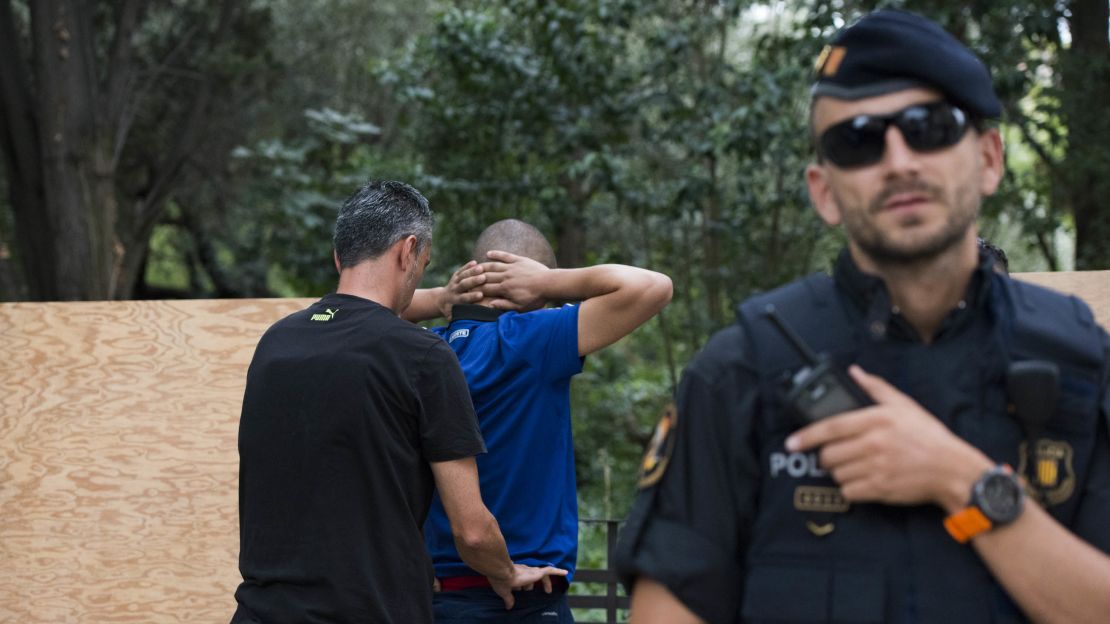 Authorities pat down a man across the street from Sagrada Familia, while mass carries on inside.