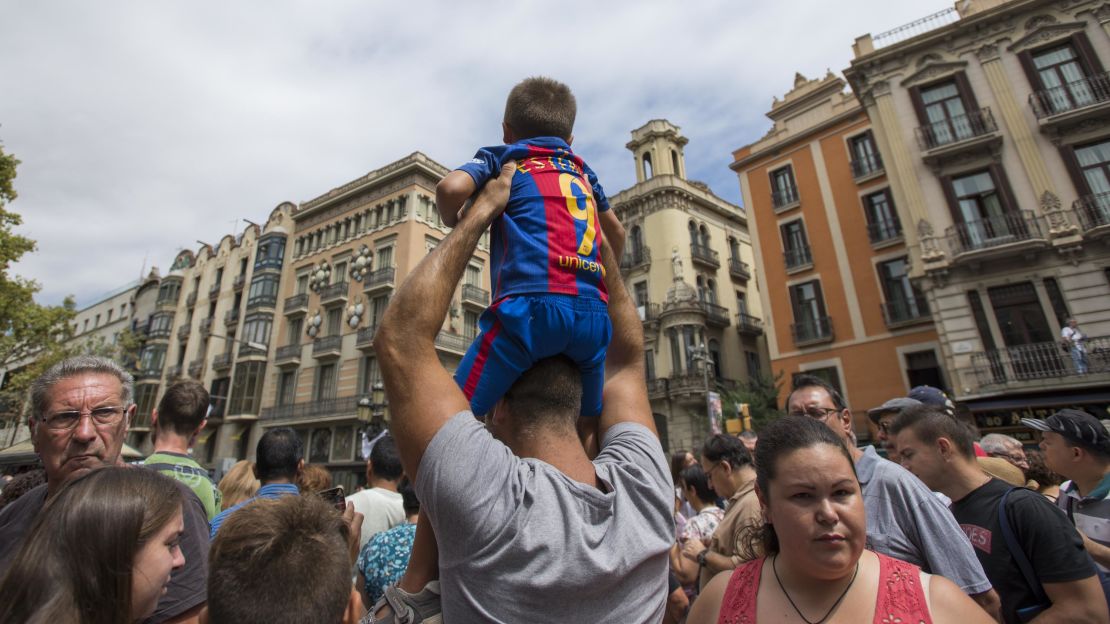 A man hoists a boy in a Barcelona football jersey above a large crowd gathered at the spot where the attacker stopped his deadly rampage.