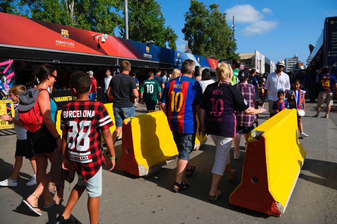 Barcelona fans pass by concrete barriers displayed at the entrance of the Camp Nou stadium.