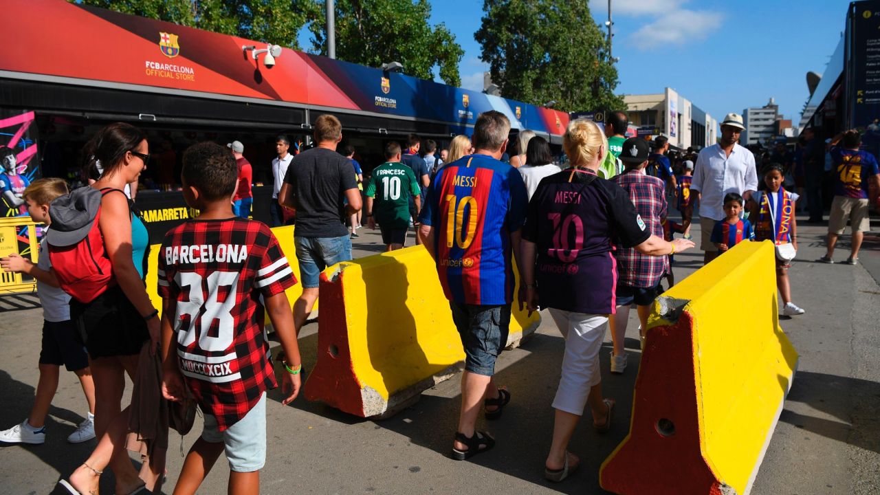 Barcelona fans pass by concrete barriers displayed at the entrance of the Camp Nou stadium.