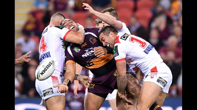 Adam Blair offloads the ball as he's crushed by members of the St. George llawarra Dragons during a rugby match in Brisbane, Australia, on Friday, August 18.