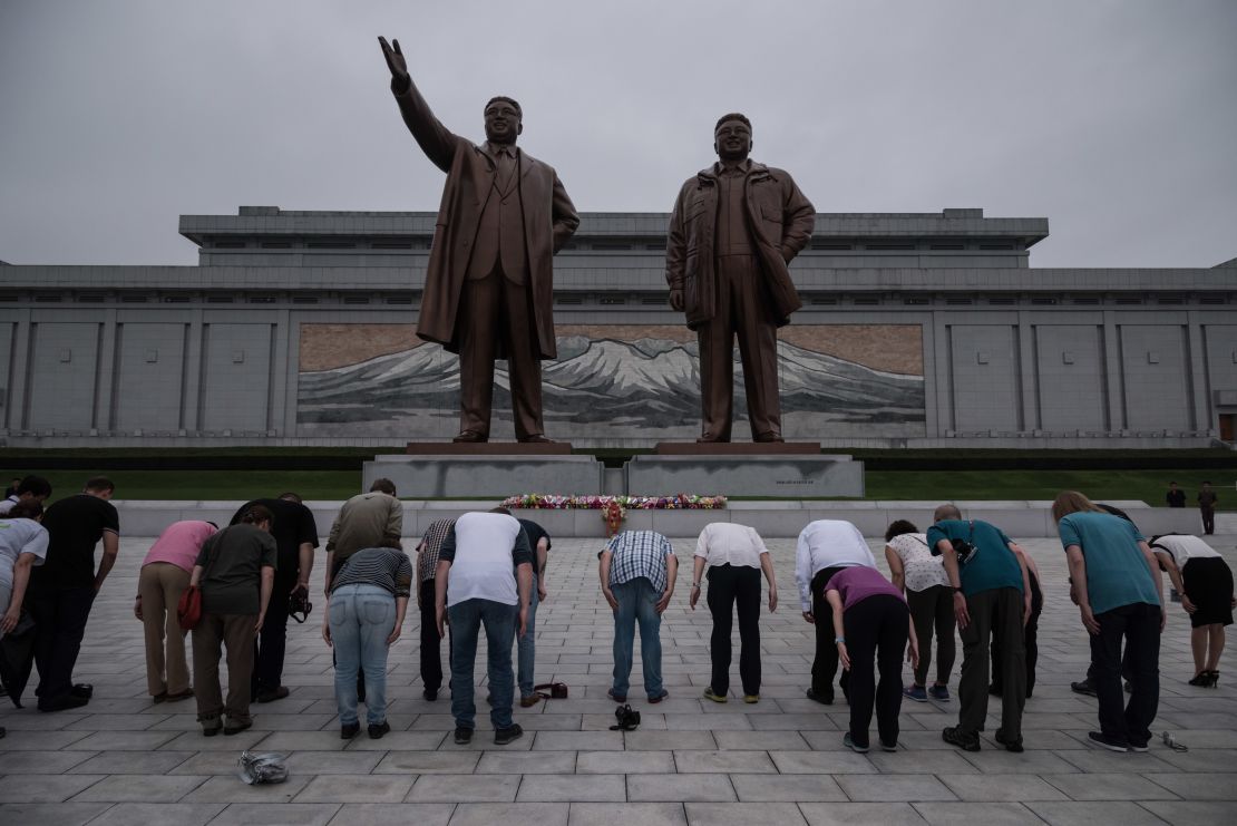 A group of tourists bow before statues of late North Korean leaders Kim Il Sung and Kim Jong Il , in Pyongyang on July 23, 2017.