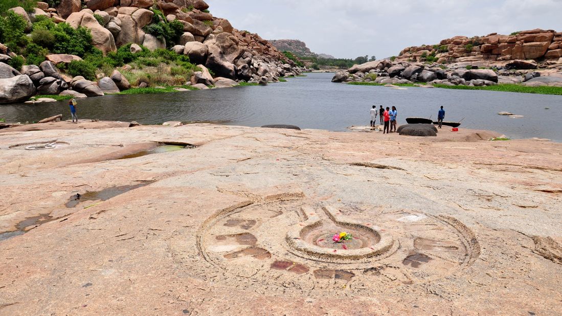<strong>Carved stone linga: </strong>An ancient yoni, symbolic of Hindu goddess Shakti, has been carved into the stone along the banks of the Tungabhadra River. In the background, boatmen await to ferry passengers across the river on their traditional coracles.