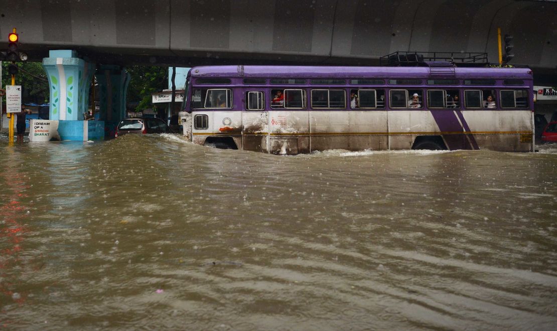 Residents are seen wading through a waterlogged street (above) while a bus tries to negotiatate another flooded road (below) in Mumbai on Tuesday. 