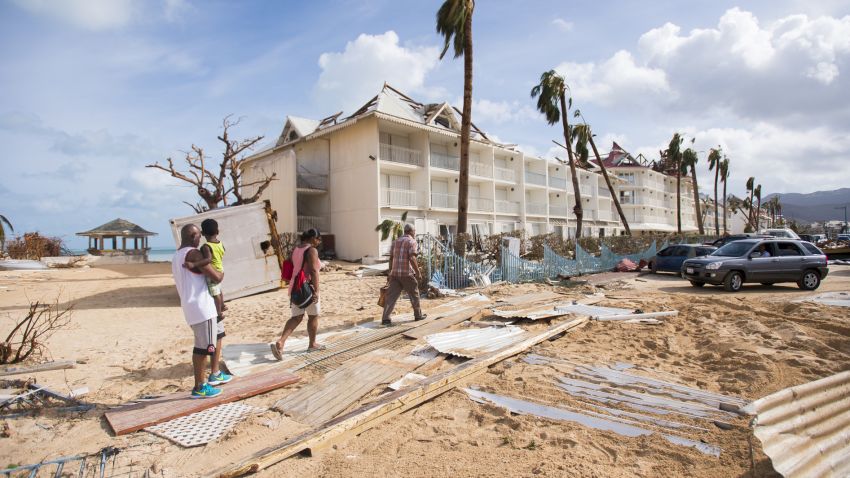 People walk through damage on September 7, in a sand-covered street of Marigot, near the Bay of Nettle, on the island of St. Martin in the northeast Caribbean, after the passage of Hurricane Irma.