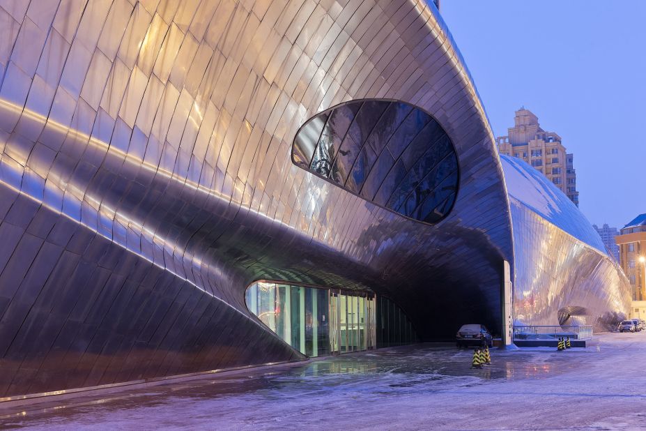 Polished metal plates on the exterior mirror the city lights at night. 