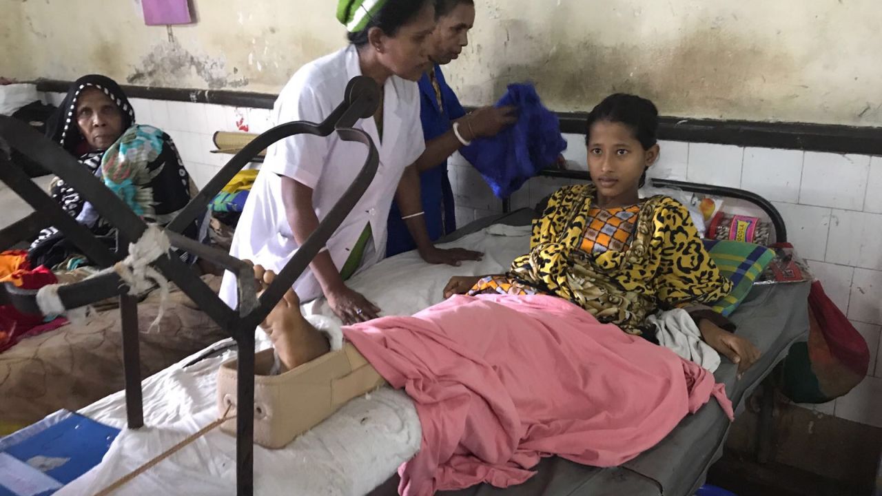 Teenager Umme Salma, who was admitted to hospital with a gunshot wound, sits up in bed with the aid of nurses.
