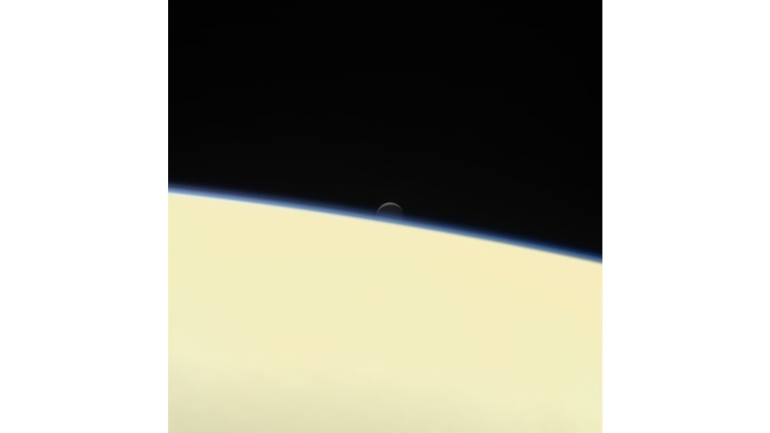 Saturn's active, ocean-bearing moon Enceladus sinks behind the giant planet in a farewell portrait from NASA's Cassini spacecraft.