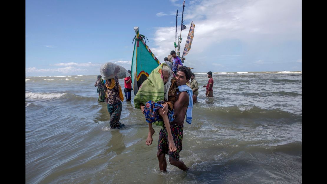 A Rohingya Muslim man walks to shore carrying an elderly woman after they arrived on a boat from Myanmar to Bangladesh.