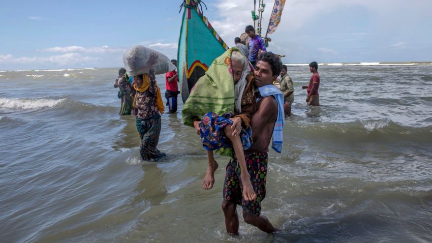 A Rohingya Muslim man walks to shore carrying an elderly woman after they arrived on a boat from Myanmar to Bangladesh in Shah Porir Dwip, Bangladesh, Thursday, Sept. 14, 2017. Nearly three weeks into a mass exodus of Rohingya fleeing violence in Myanmar, thousands were still flooding across the border Thursday in search of help and safety in teeming refugee settlements in Bangladesh. Those who arrived Wednesday in wooden boats described ongoing violence in Myanmar, where smoke could be seen billowing from a burning village, suggesting more Rohingya homes had been set alight. (AP Photo/Dar Yasin)