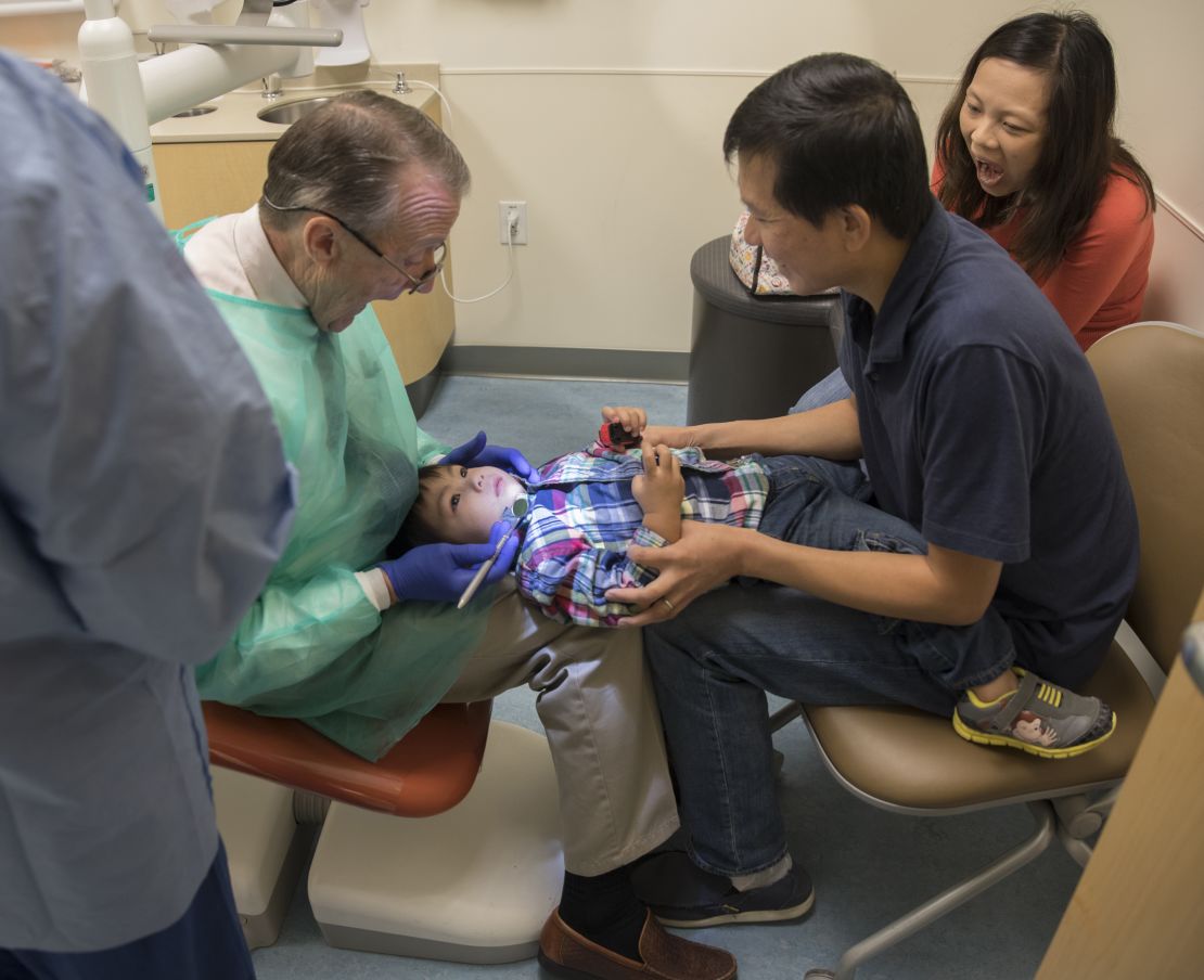Ray Stewart, a pediatric dental professor at the University of California-San Francisco, examines Matthew Mai, 2, with the help of his parents, Sean and Tina Mai.