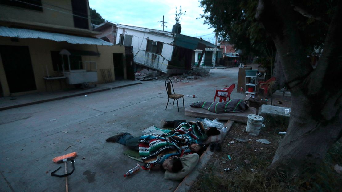 People are sleeping on the street next to homes damaged by the earthquake.