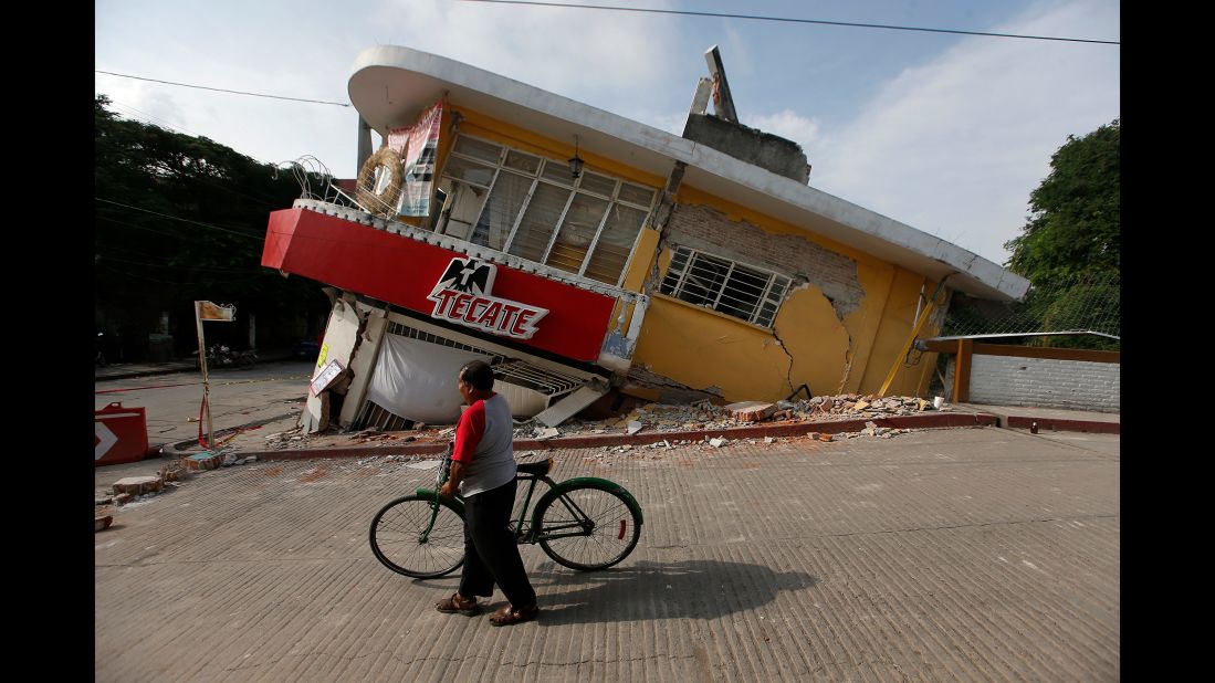 A man walks his bike past a partially collapsed building in Jojutla on September 20.