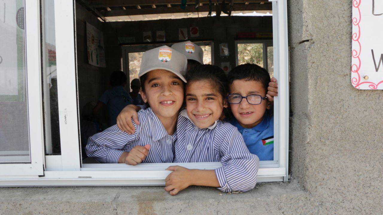 Nine-year-old Sundus Zawahra, left, and eight-year-old Nagham Ali, right, peer through the window of their fourth grade class with a friend at the school.