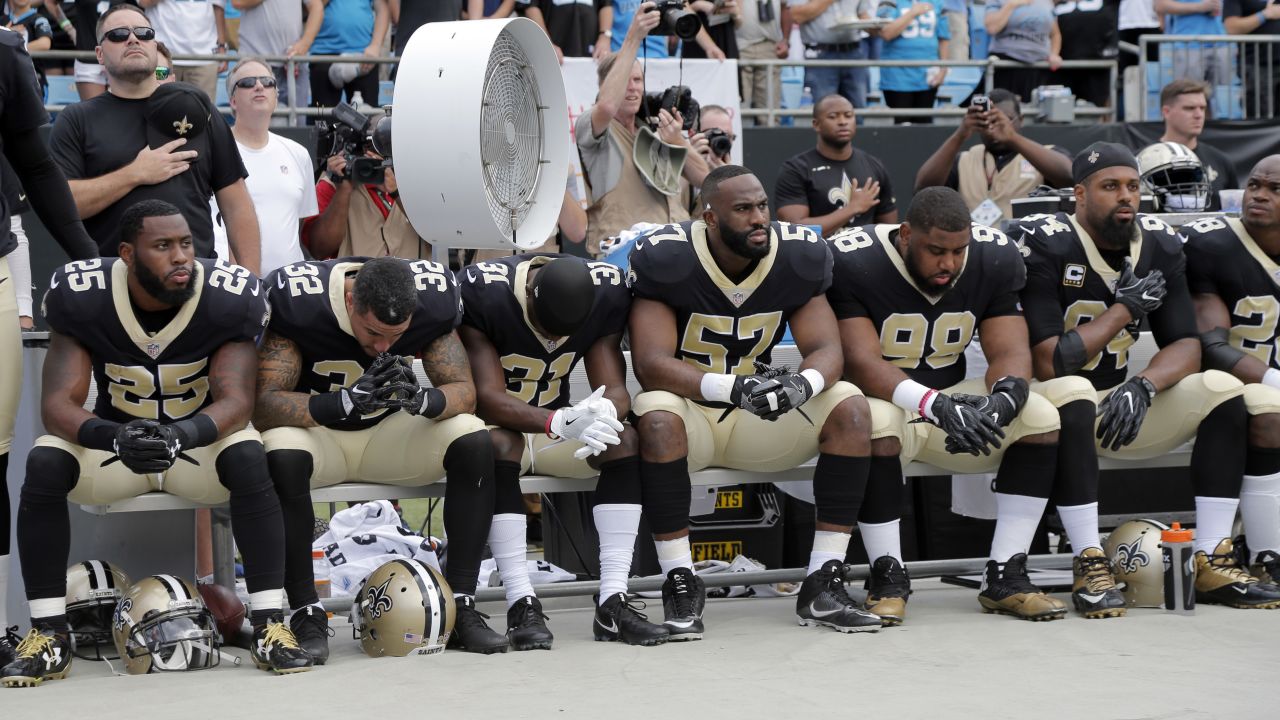 New Orleans Saints players sit on the bench during the national anthem before a game against the Carolina Panthers.