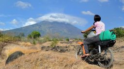 TOPSHOT - A girl rides a motorbike in the Kubu subdistrict of Karangasem Regency on the Indonesian resort island of Bali on September 26, 2017, as Mount Agung volcano looms in the background.
More than 57,000 people have fled a volcano on the tourist island of Bali as rising magma and increased tremors fuel fears of an imminent eruption, officials said on September 26. / AFP PHOTO / SONNY TUMBELAKA        (Photo credit should read SONNY TUMBELAKA/AFP/Getty Images)