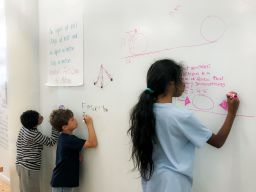 Children independently problem solve on walls made of whiteboards. 