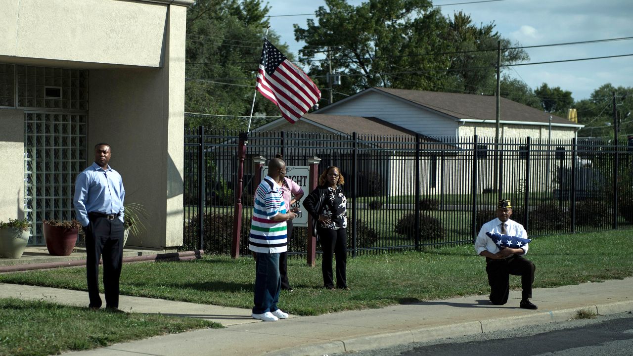 A man takes a knee while holding an American flag as a motorcade with US President Donald Trump drives to Indianapolis International Airport September 27, 2017 in Indianapolis, Indiana. / AFP PHOTO / Brendan Smialowski        (Photo credit should read BRENDAN SMIALOWSKI/AFP/Getty Images)