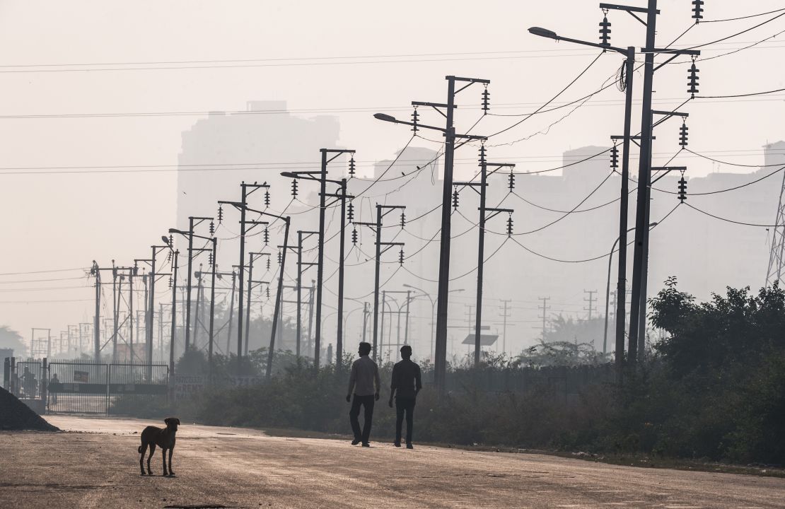 Two Indian men walk past electricity wires near newly built residential towers in Noida, a satellite city of New Delhi. 