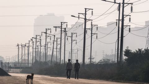 Two Indian men walk past electricity wires near newly built residential towers in Noida, a satellite city of New Delhi. 