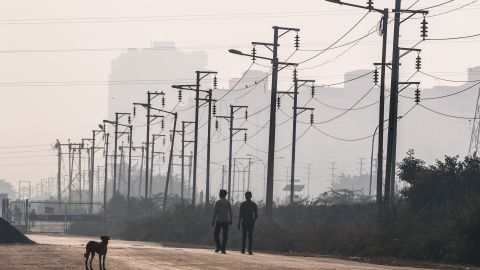 Two Indian men walk past electricity wires near newly built residential towers in Noida, a satellite city of New Delhi.
