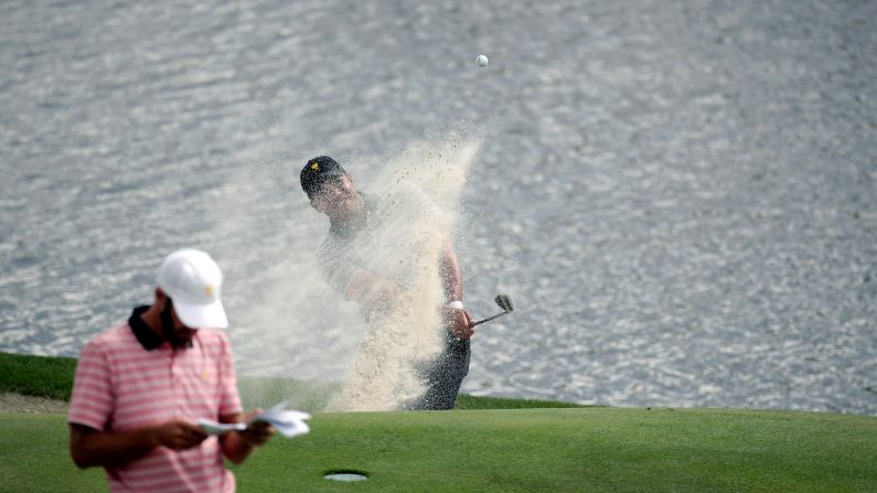 Jhonattan Vegas, rear, hits from a bunker as Dustin Johnson, left, waits on the seventh green during the four-ball golf matches on the second day of the Presidents Cup at Liberty National Golf Club in Jersey City, N.J., Friday, Sept. 29, 2017. (AP Photo/Julio Cortez)