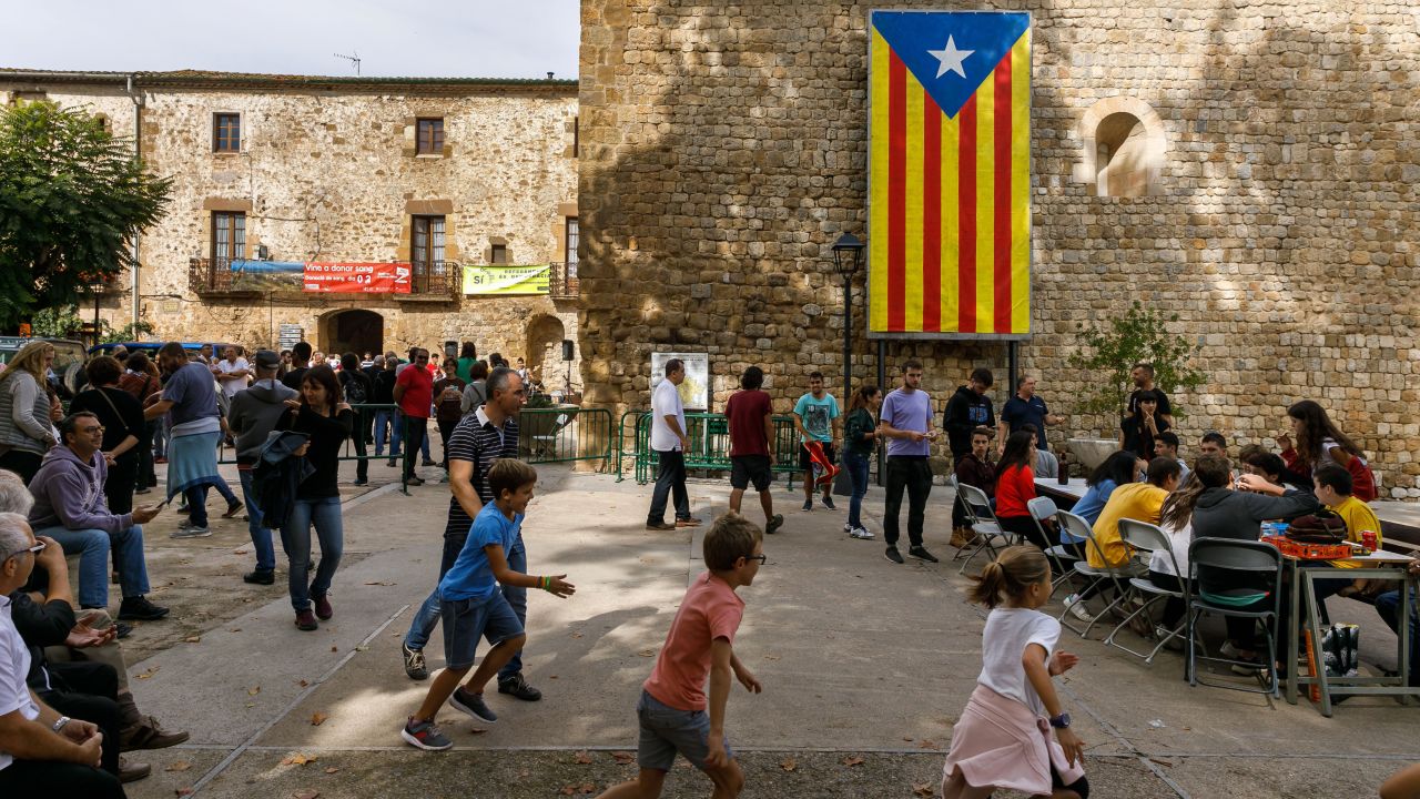 People play games in a square where a giant pro-independence Estelada Catalan flag is displayed.