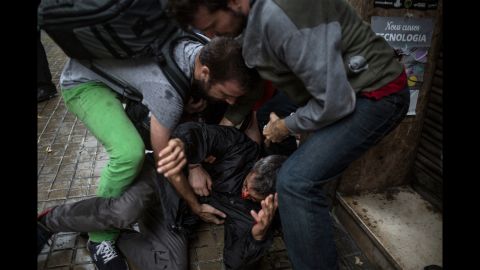 People help a man injured by a rubber bullet fired by Spanish police officers outside the Ramon Llull polling station in Barcelona.