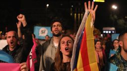 A woman holds a Catalan flag as crowds listen to Catalan President Carles Puigdemont speak via a televised press conference as they await the result of the Indepenence Referendum at the Placa de Catalunya on October 1 in Barcelona.