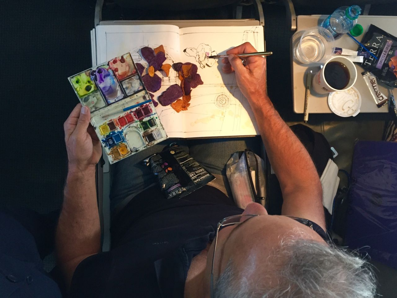 Gardner, pictured here painting on board a plane, tries his best to sketch in all conditions.