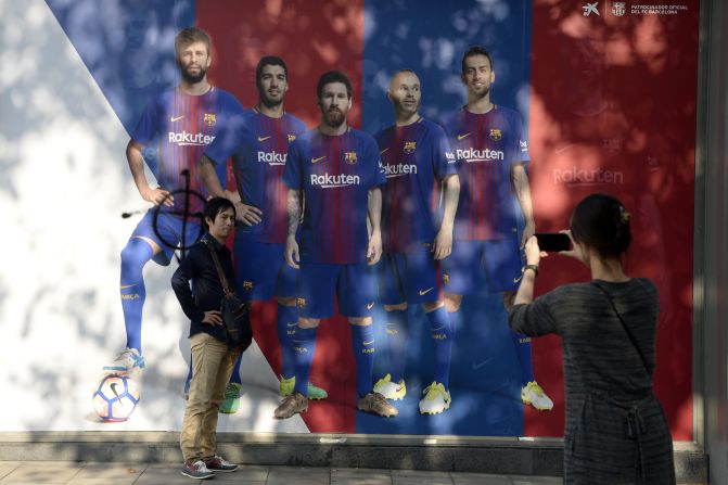A fan poses in front of a poster of Barcelona  where the picture of defender Gerard Pique has been vandalized outside the club's Camp Nou stadium which was closed as part of a general strike in Barcelona called by Catalan unions on October 3, 2017.Several hundred thousand Catalans rallied in fury at police violence against voters during a banned independence referendum, as Madrid accused regional authorities of "inciting rebellion". Barcelona football club refused to train as part of an accompanying strike, which officials said slowed down public transport and freight shipments in the port of Barcelona. Pique is an outspoken defender of the wealthy northeastern Spanish region's right to self-determination.