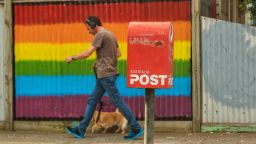 A man walk his dog past a Rainbow painted fence next to a post office box. Australians are not voting either Yes or No in the Same Sex Marriage Survey.