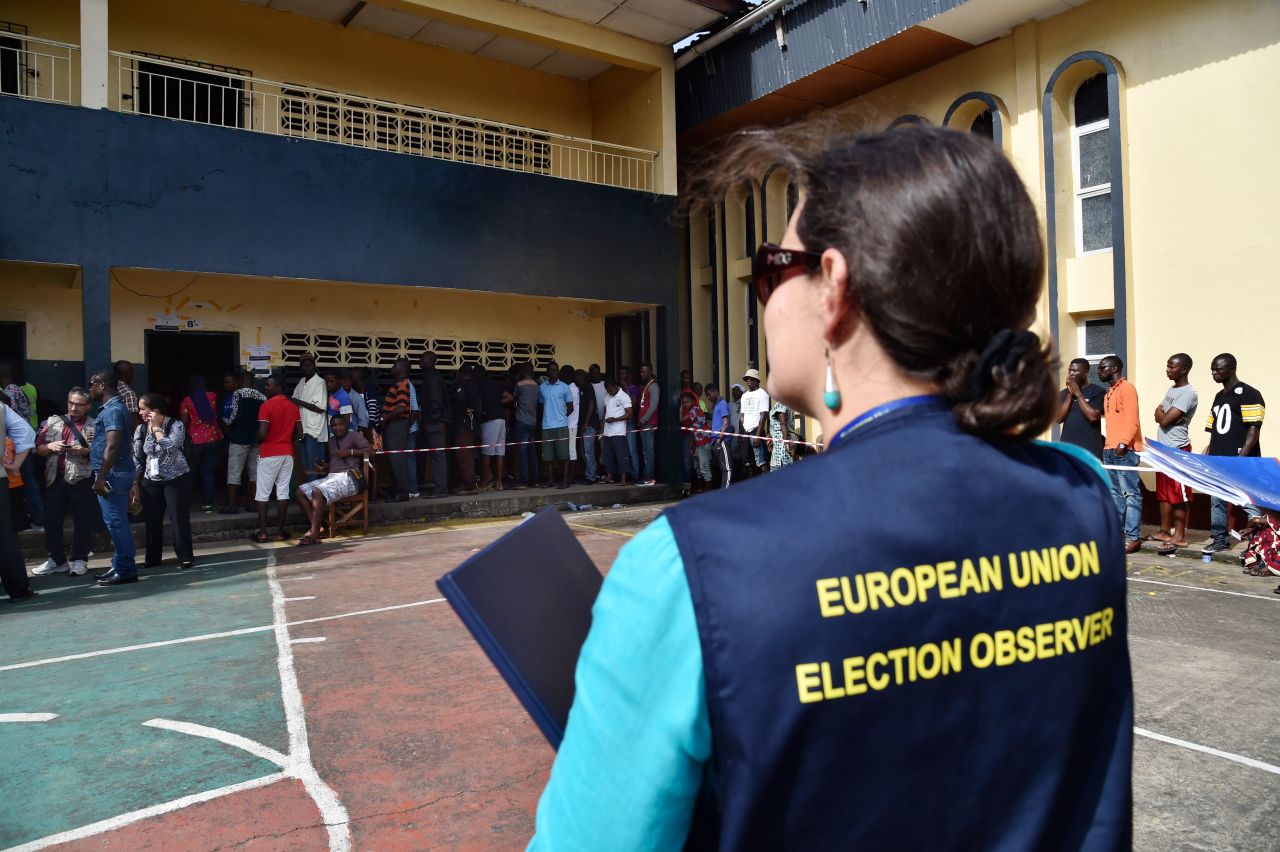 A European Union election observer stands near voters queuing at a polling station in Monrovia. <br />Credit: Getty images