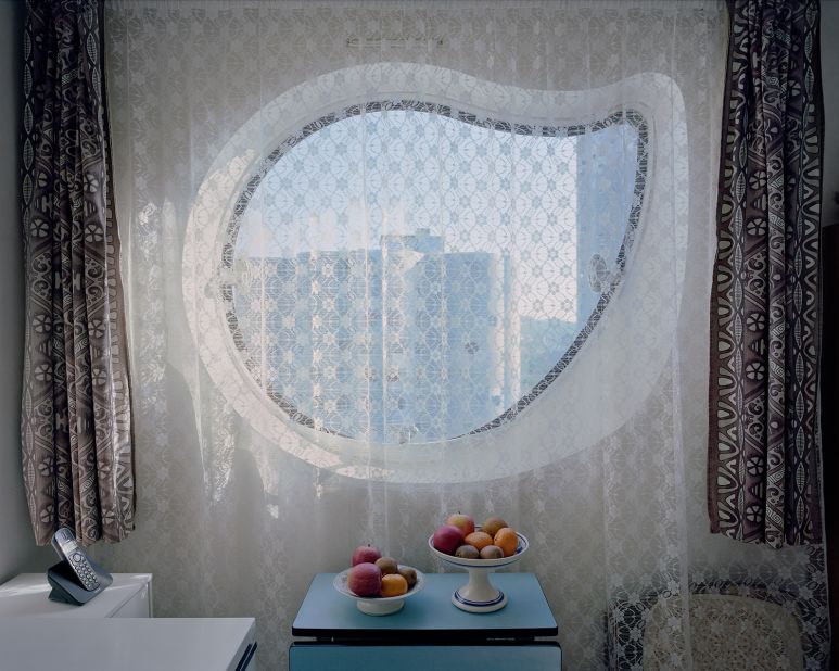 "[In this photo] we are in the kitchen of a senior couple. The curtain slightly shrouds the outside, a soft light wraps the room, the two fruit baskets on the table catch your eye. Everything appears motionless, and nothing seems to have changed. Is it a throwback to the years 1970-80 when Emile Aillaud's work was completed, when the first inhabitants came to live in the towers? The telephone is the only sign which allows to situate the date of shooting. This is actually 2017." 