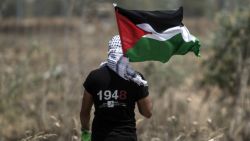 TOPSHOT - A Palestinian youth waves the national flag as Israeli military digs in search of smuggling tunnels at the border east of Gaza city on May 15, 2016, on the 68th anniversary of the "Nakba".
"Nakba" means in Arabic "catastrophe" in reference to the birth of the state of Israel 68-years-ago in British-mandate Palestine, which led to the displacement of hundreds of thousands of Palestinians who either fled or were driven out of their homes during the 1948 war over Israel's creation.
 / AFP / MAHMUD HAMS        (Photo credit should read MAHMUD HAMS/AFP/Getty Images)
