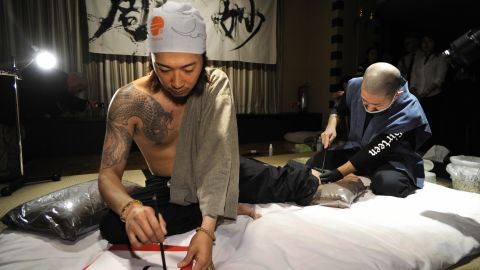 Japanese calligrapher Hayato Suzuki writes Chinese characters while tattoo artist Horimyo (right) tattoos on his leg in Tokyo in 2009.  