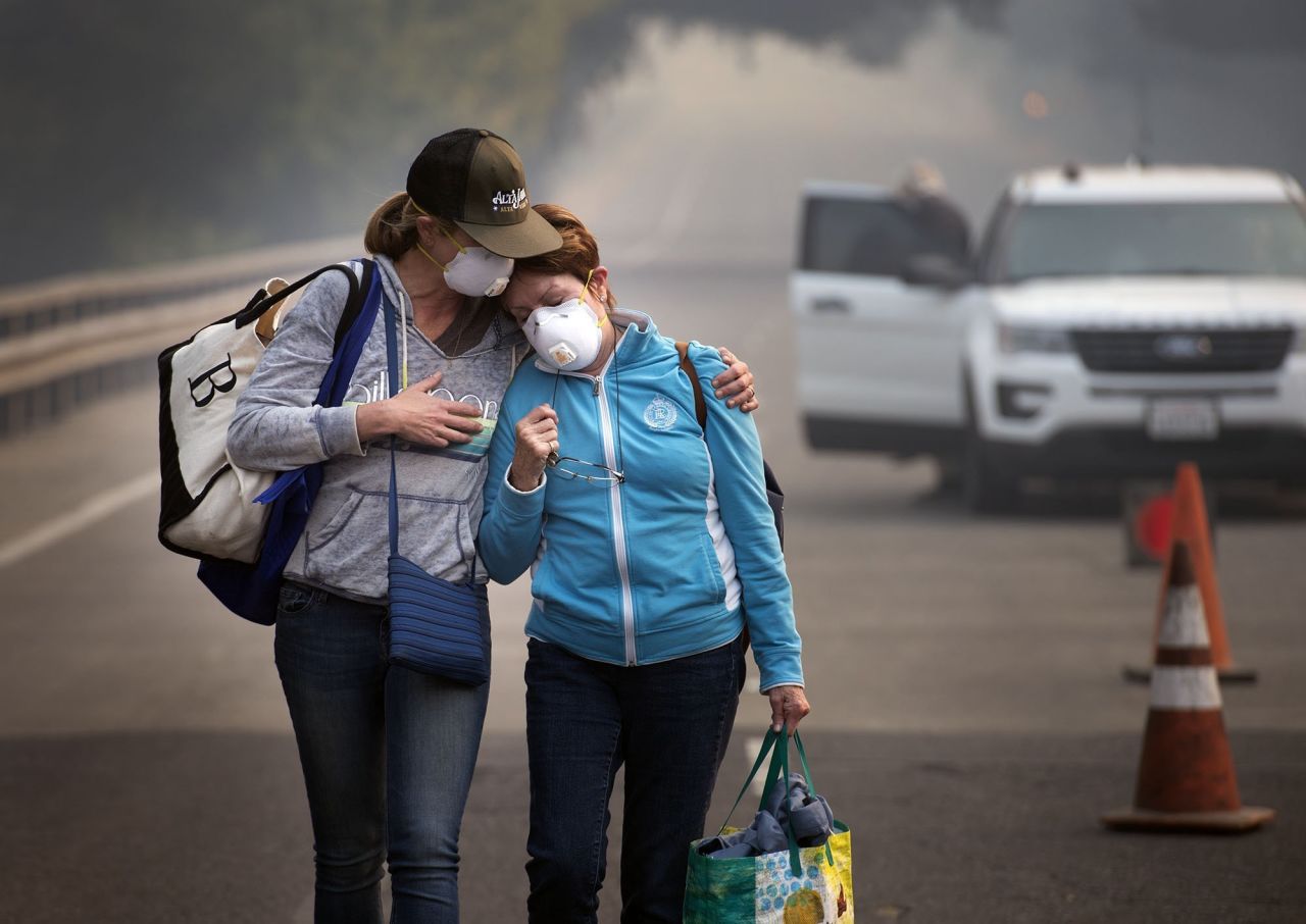 Colby Clark, left, comforts her mother, Bonnie Trexler, after law enforcement escorted them to Trexler's home in Napa, California, to retrieve medicine and personal items on Wednesday, October 11. Trexler was one of the lucky few in her neighborhood whose home was spared. Deadly wildfires have been tearing through the state, destroying homes and businesses and prompting evacuation orders.