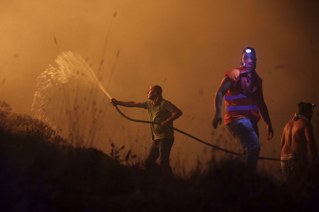 Volunteers use a water hose to fight a fire raging near houses in the outskirts of Obidos, Portugal.