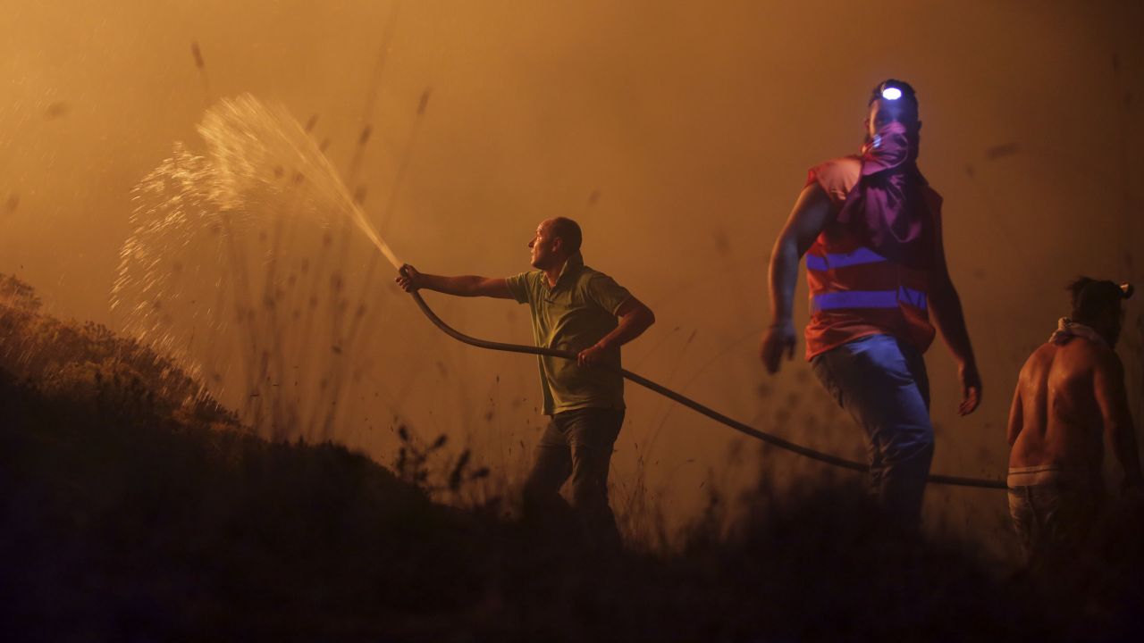 Volunteers use a water hose to fight a fire raging near houses in the outskirts of Obidos, Portugal.