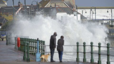 A couple watch waves break on the sea wall at Penzanze, southwestern England, on October 16, 2017.