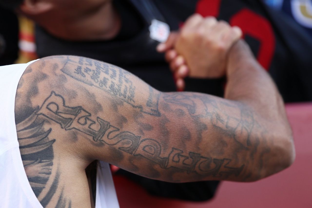 The upper half of NFL star Colin Kaepernick's right arm is covered in ink, as is most of his torso. Across his chest is written "Against All Odds" while down his arm is the word "Respect."