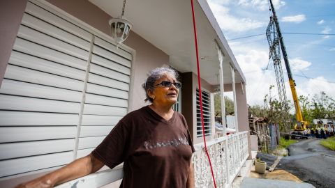 Diana Aponte stands by her home in Aguas Buenas, next to the reconstruction of a transmission tower.