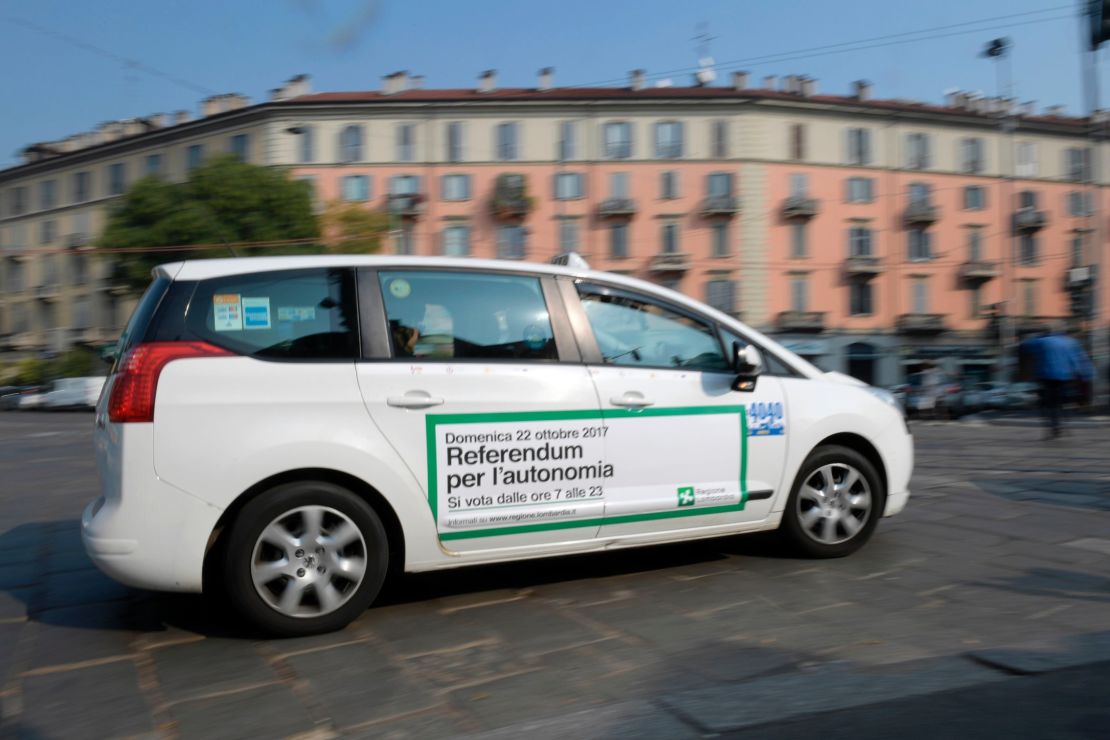 A taxi with a sticker announcing the Lombardy referendum passes along a street in Milan.
