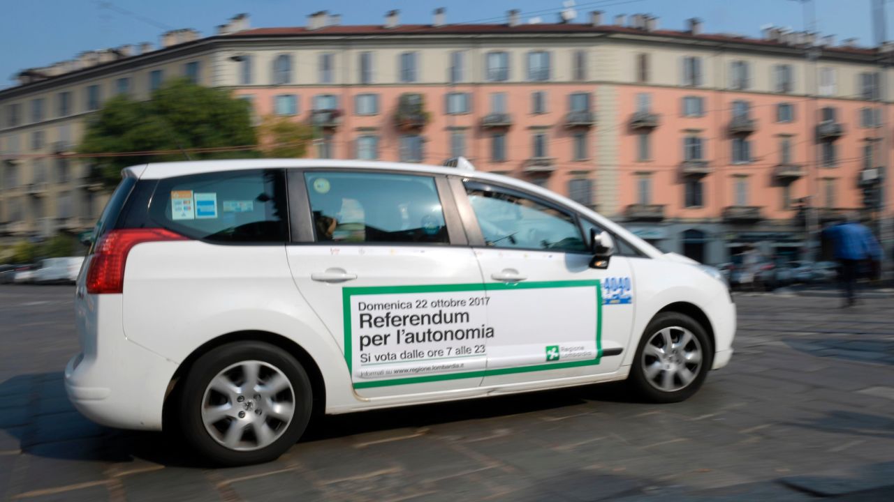 A taxi with a sticker announcing the Lombardy referendum passes along a street in Milan.