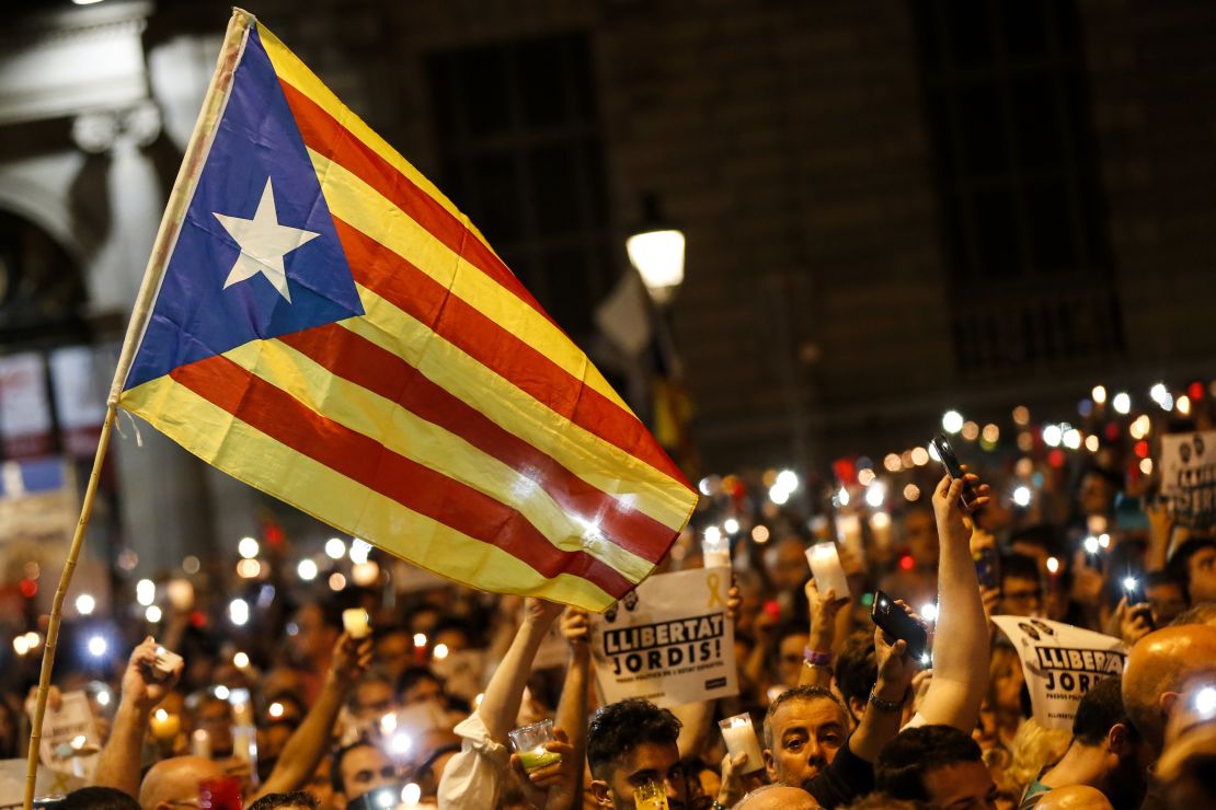 People hold candles and a Catalan pro-independence 'Estelada' flag during a demonstration in Barcelona against the arrest of two Catalan separatist leaders on October 17, 2017.