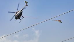 A helicopter hoists workers to fix power lines in Puerto Rico's mountains.