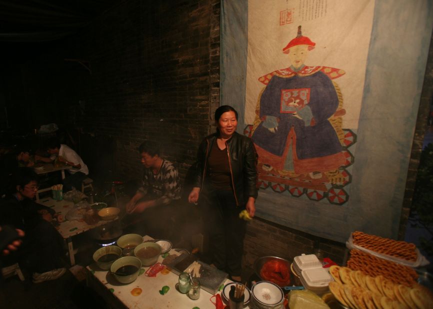 A street vendor sets out her wares under a painting of a Qing Dynasty official. 