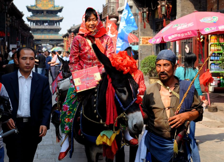A bride dressed in traditional red robes rides a donkey through Pingyao's ancient streets. 