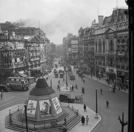 A view of Piccadilly Circus, London, at the height of World War II in 1942. Eros can be seen in the foreground, sand-bagged and covered in War Savings posters and the Criterion Restaurant is visible on the right. The buildings are covered with advertisements.